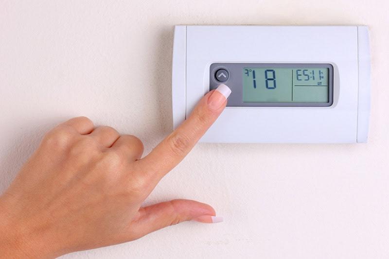 A female hand reaching to set the temperature lower on a thermostat.